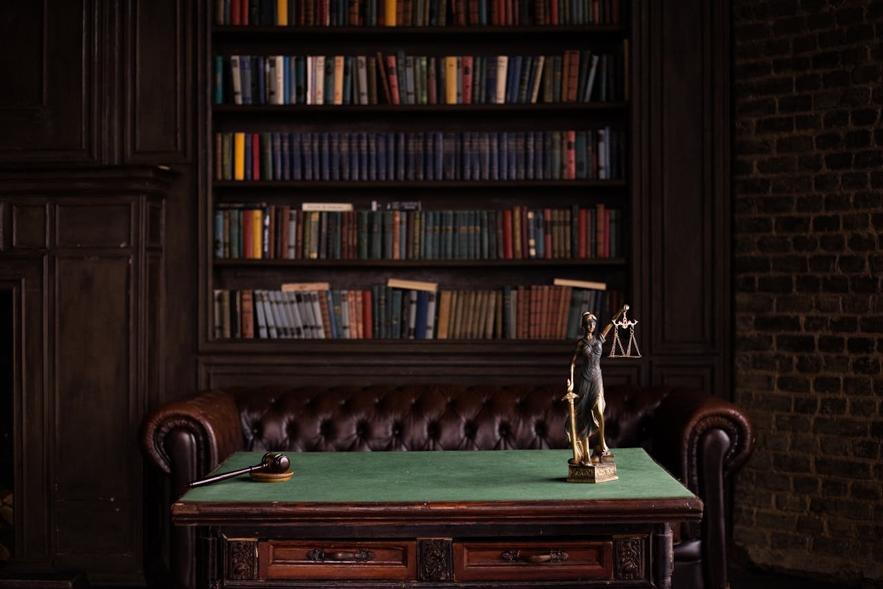 Abogada La Garriga Barcelona. A classic study room with shelves of books, a gavel, and Lady Justice figurine on a green table.