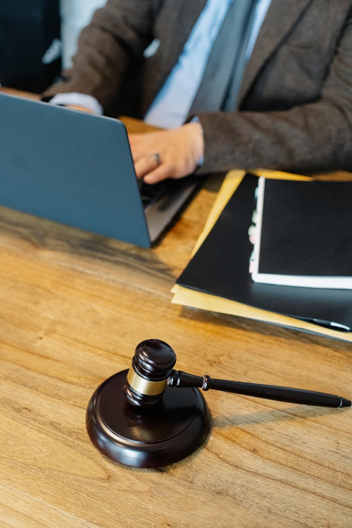 Servicios legales en La Garriga. From above of crop anonymous male lawyer in formal clothes typing on laptop while sitting at wooden table with stack of documents and gavel